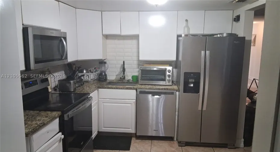 Kitchen featuring white cabinetry, stainless steel appliances, speckled stone-finish countertops, and a white subway tile backsplash