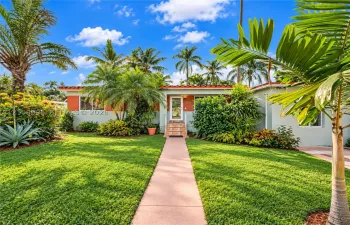 Single-story exterior featuring a clay tile roof, concrete walkway, landscaped lawn, and mature palm trees