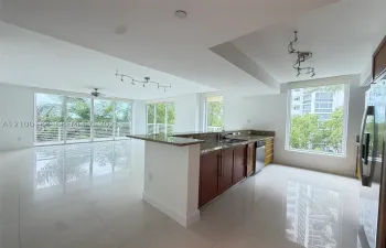 Open concept kitchen featuring stone countertops, wood-finish cabinetry, stainless steel appliances, large-format tile flooring, and floor-to-ceiling windows