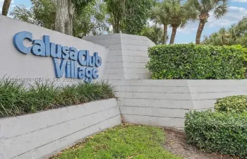 Monument signage for Calusa Club Village featuring a tiered concrete structure, integrated landscaping, and mature palms