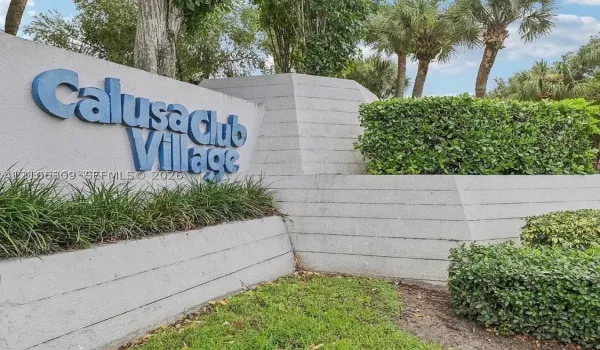 Monument signage for Calusa Club Village featuring a tiered concrete structure, integrated landscaping, and mature palms