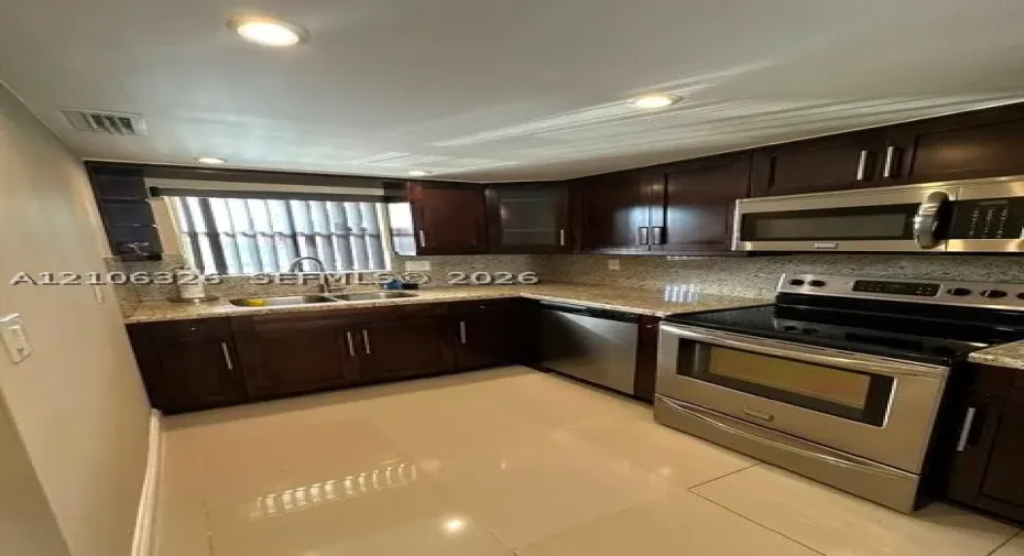 Kitchen featuring dark-finish cabinetry, stone-surfaced countertops, stainless steel appliances, recessed ceiling lighting, and tile flooring