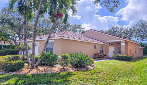 Stucco exterior featuring a hipped tile roof, integrated garage, covered entryway, and mature tropical landscaping