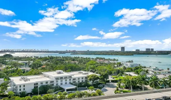 Aerial perspective of coastal property featuring multi-story white building, lush tropical landscaping, paved motor court, and extensive water frontage