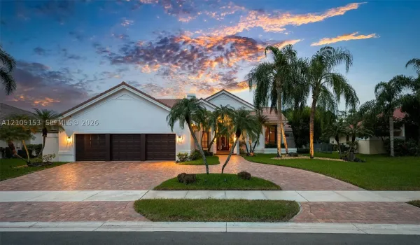 Stucco exterior with a tile roof, paver driveway, three-car garage, and established palm trees