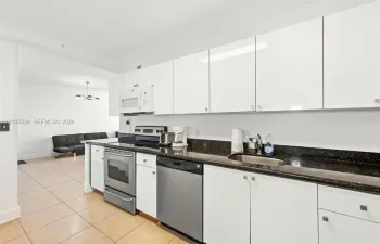 Modern kitchen with sleek white cabinetry, dark stone countertops, stainless steel appliances, and tile flooring