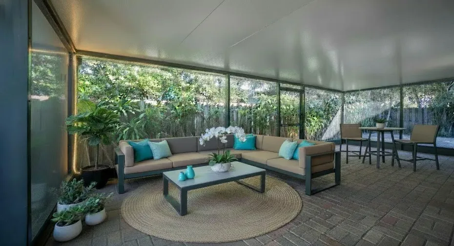 Screened outdoor living area with a solid roof, brick paver flooring, and abundant natural light