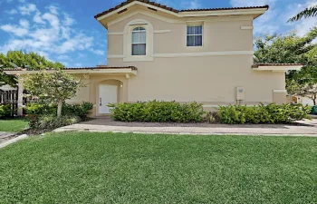 Two-story stucco exterior featuring a tiled roof, arched window detailing, and an integrated paver walkway