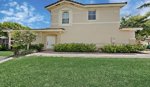 Two-story stucco exterior featuring a tiled roof, arched window detailing, and an integrated paver walkway