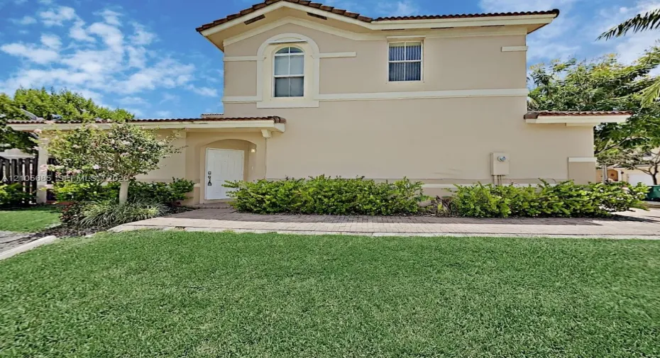 Two-story stucco exterior featuring a tiled roof, arched window detailing, and an integrated paver walkway
