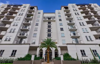 Multi-story stucco exterior featuring symmetrical design, private balconies with decorative metal railings, decorative roof pergolas, and palm-accented entrance hardscaping