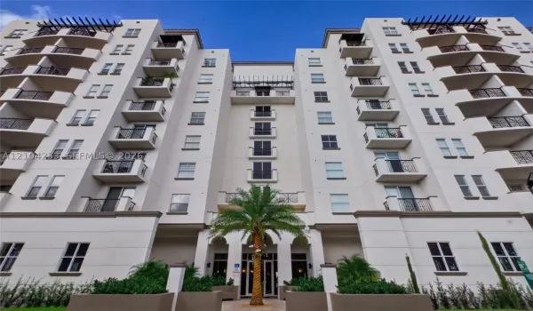 Multi-story stucco exterior featuring symmetrical design, private balconies with decorative metal railings, decorative roof pergolas, and palm-accented entrance hardscaping