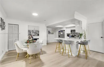 Light wood-finish flooring throughout, white walls, recessed lighting, and a white kitchen island with counter seating