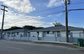 Single-story structure featuring a concrete exterior, multi-hipped shingle roof, and a perimeter concrete wall with integrated metal fencing