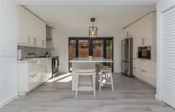 Kitchen featuring white cabinetry, center island with stone countertop, apron-front sink, stainless steel appliances, and wood-finish flooring