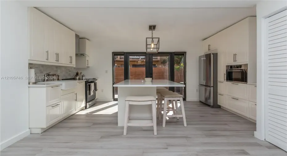 Kitchen featuring white cabinetry, center island with stone countertop, apron-front sink, stainless steel appliances, and wood-finish flooring