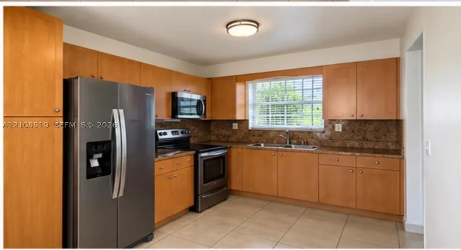 Kitchen featuring light wood-finish cabinetry, stainless steel appliances, a double basin sink, and tile flooring