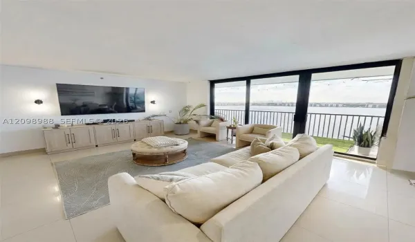 Living area featuring floor-to-ceiling glass sliding doors, integrated cabinetry, polished tile flooring, and a metal-railed balcony with waterfront exposure