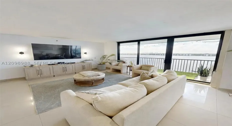 Living area featuring floor-to-ceiling glass sliding doors, integrated cabinetry, polished tile flooring, and a metal-railed balcony with waterfront exposure
