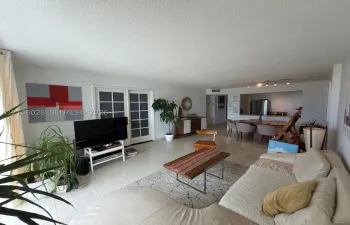 Living area featuring large-format tile flooring, multi-pane glass sliding doors, and an open pass-through window to the kitchen area