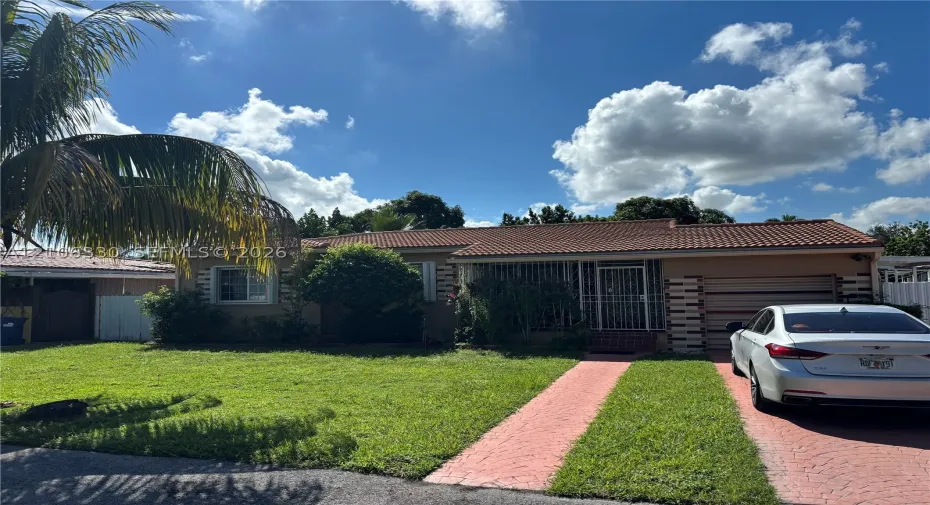 Single-story exterior featuring a clay tile roof, stucco siding, and a paved ribbon driveway