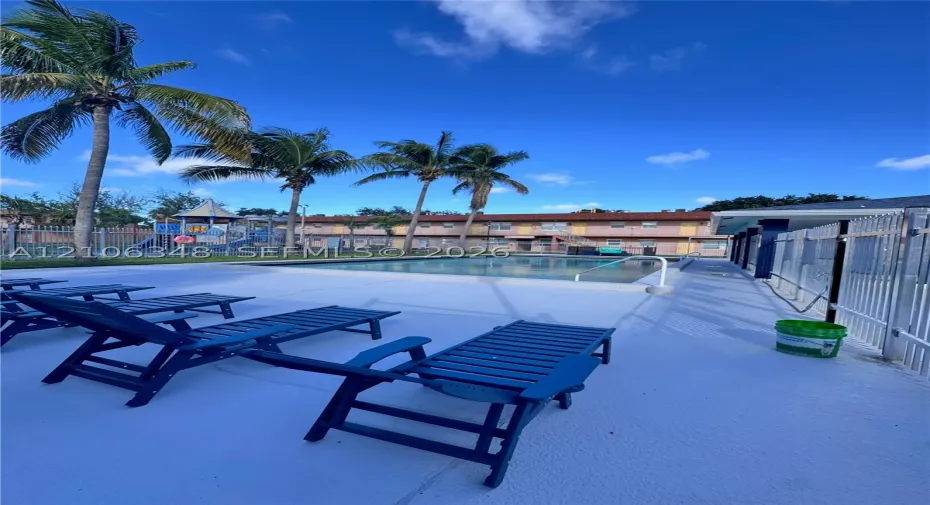 In-ground swimming pool featuring a concrete deck and metal perimeter fencing, accented by mature palm trees