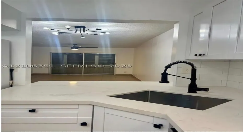 Kitchen featuring white shaker-style cabinetry, solid-surface countertops, a stainless steel undermount sink with a matte black pull-down faucet, and a white subway tile backsplash
