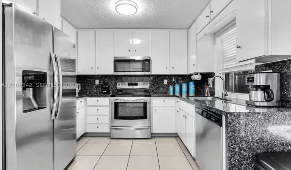 Kitchen featuring white cabinetry, dark stone-finish countertops, stainless steel appliances, ceramic tile flooring, and a single-basin undermount sink with a pull-down faucet