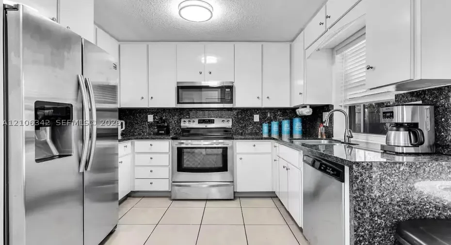 Kitchen featuring white cabinetry, dark stone-finish countertops, stainless steel appliances, ceramic tile flooring, and a single-basin undermount sink with a pull-down faucet