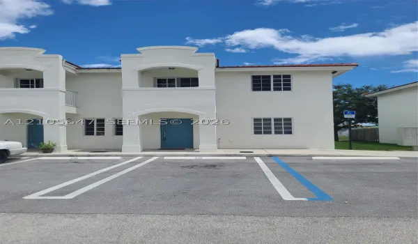 Two-story stucco exterior featuring arched entryway detailing, a covered second-story balcony, multi-pane windows, and dedicated asphalt parking