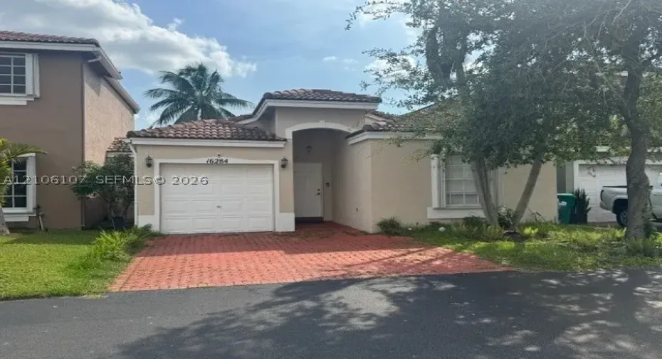 Stucco exterior with a tiled roof, arched entryway, and patterned paver driveway featuring an attached garage