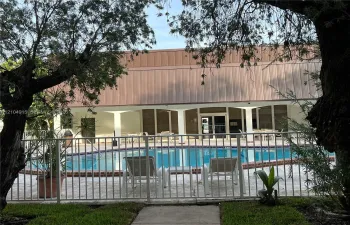 Swimming pool with brick coping, surrounded by a paved deck and enclosed by a metal perimeter fence, featuring a covered patio with structural columns