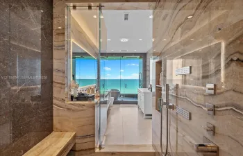 Walk-in shower clad in polished natural stone, featuring a built-in stone bench, integrated recessed shelving, multi-head shower system, and glass enclosure