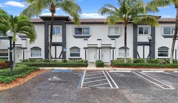 Two-story townhome exterior featuring stucco siding with contrasting trim, arched window accents, tiled roof, and manicured landscaping
