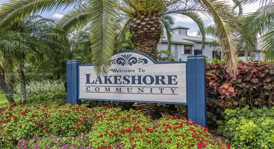 Lakeshore Community entrance signage featuring wood-frame construction, set within professional landscaping comprised of palm trees and flowering shrubs
