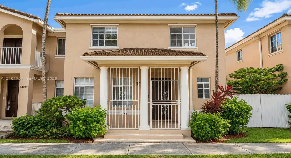 Two-story stucco facade featuring a covered entry porch with columns, tile roofing, and white-framed windows