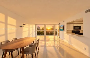 Open-concept interior featuring large-format tile flooring, expansive floor-to-ceiling windows, and a kitchen pass-through with a built-in breakfast bar