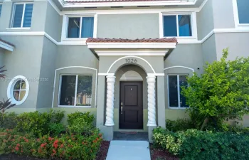 Stucco exterior featuring an arched entryway with decorative spiral columns, a portico with tile roofing, and a circular accent window