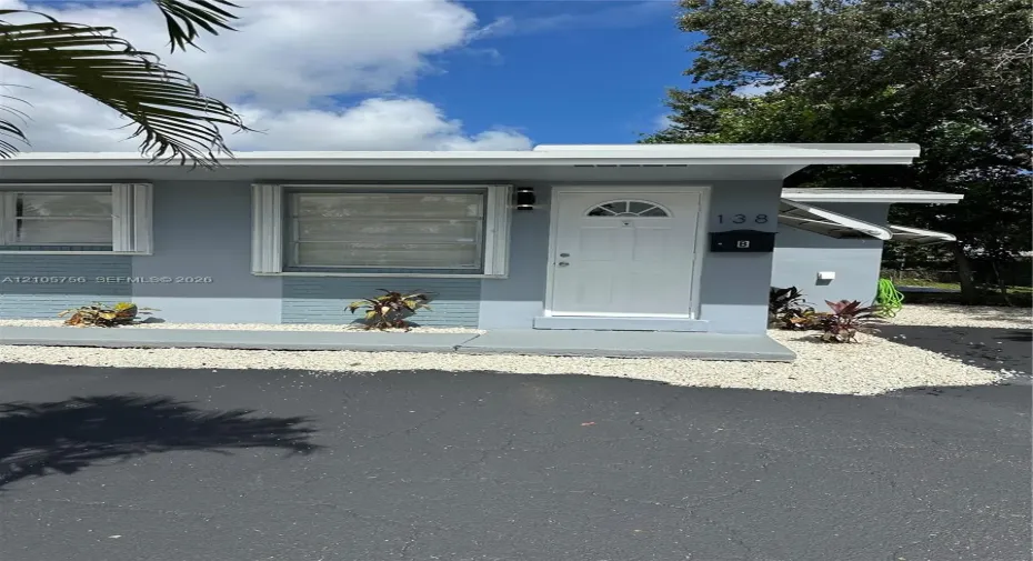 Exterior featuring a painted masonry facade, white entry door with glass insert, horizontal sliding windows, and a concrete stoop with gravel landscaping