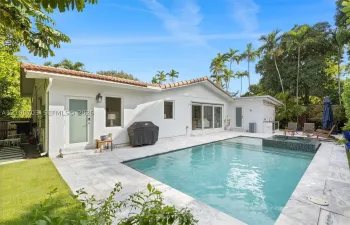 Backyard area featuring an in-ground swimming pool, attached tiled spa, stone paver decking, and exterior wall-mounted lighting