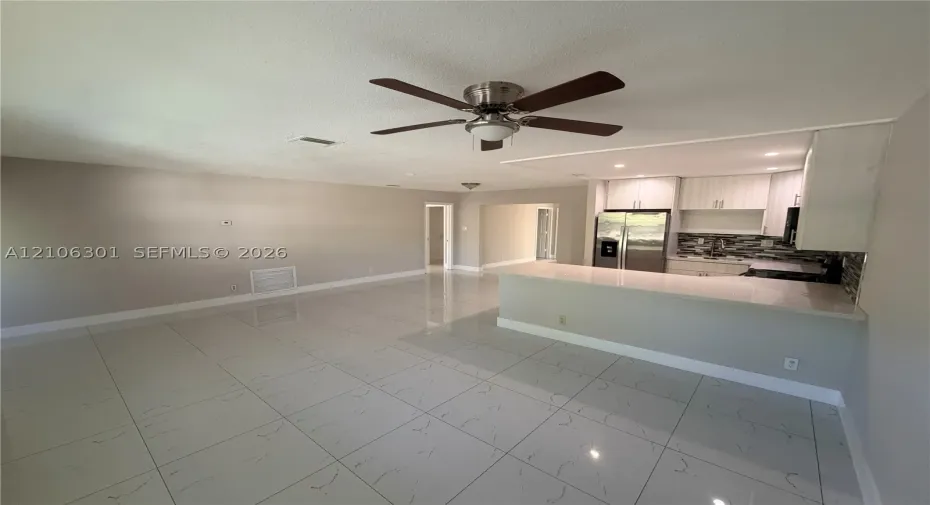 Large-format tile flooring, kitchen peninsula with a stone-surface countertop, white cabinetry, integrated stainless steel appliances, and a ceiling fan