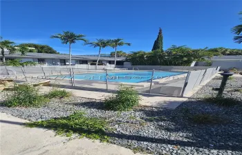 Swimming pool featuring a rectangular design, mesh perimeter fencing, and concrete decking, surrounded by stone landscaping and mature palm trees
