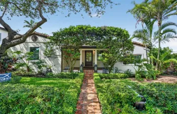 Stucco exterior residence featuring a clay tile roof, brick walkway, and landscaped garden beds