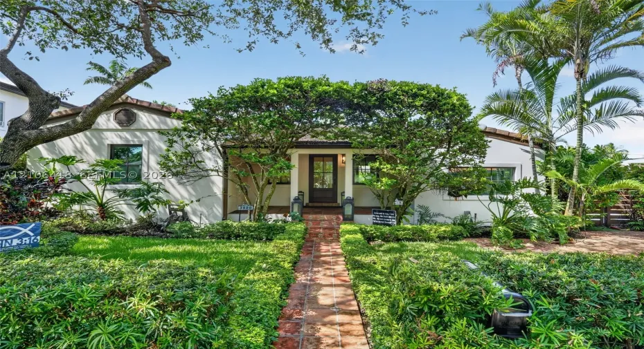 Stucco exterior residence featuring a clay tile roof, brick walkway, and landscaped garden beds