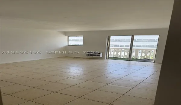 Neutral-toned ceramic tile flooring, sliding glass door with balcony access, and wall-mounted climate control unit