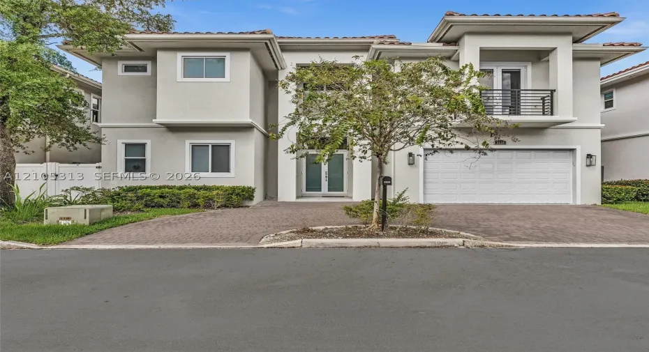 Two-story stucco exterior featuring a paved driveway, integrated two-car garage, upper-level balcony with metal railing, and double-entry doors