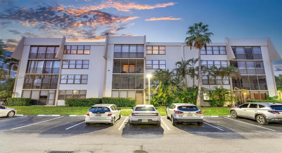 Multi-story residential building featuring a reinforced concrete facade, screened-in balconies, large grid windows, and established tropical landscaping