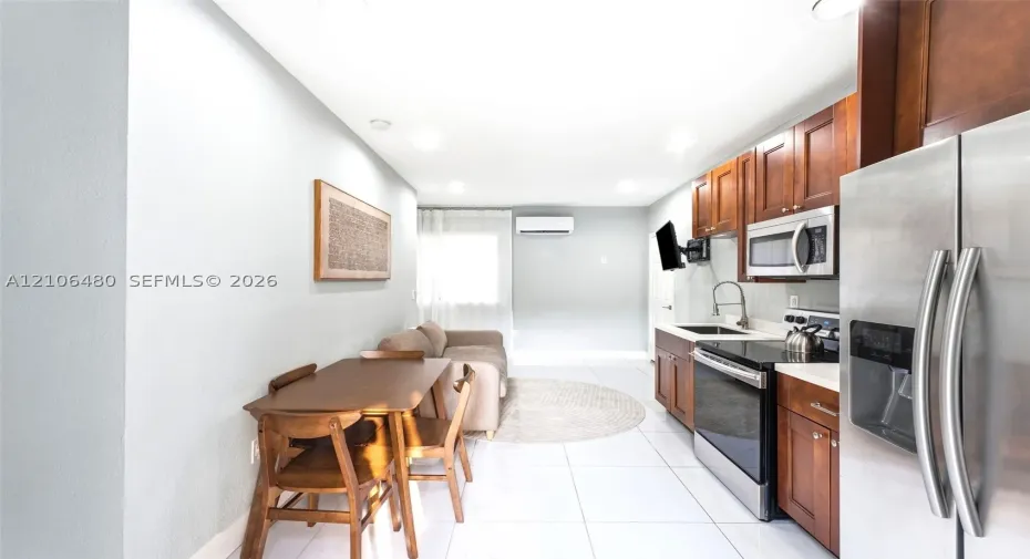 Kitchen featuring cherry-toned cabinetry, stainless steel appliances, a gooseneck faucet, tile flooring, and a wall-mounted climate control unit