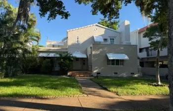 Stucco exterior residence featuring a tiled chimney, decorative geometric window accents, metal window awnings, and a brick-stepped entryway