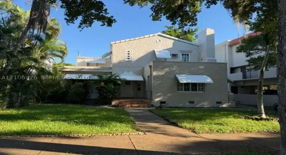 Stucco exterior residence featuring a tiled chimney, decorative geometric window accents, metal window awnings, and a brick-stepped entryway